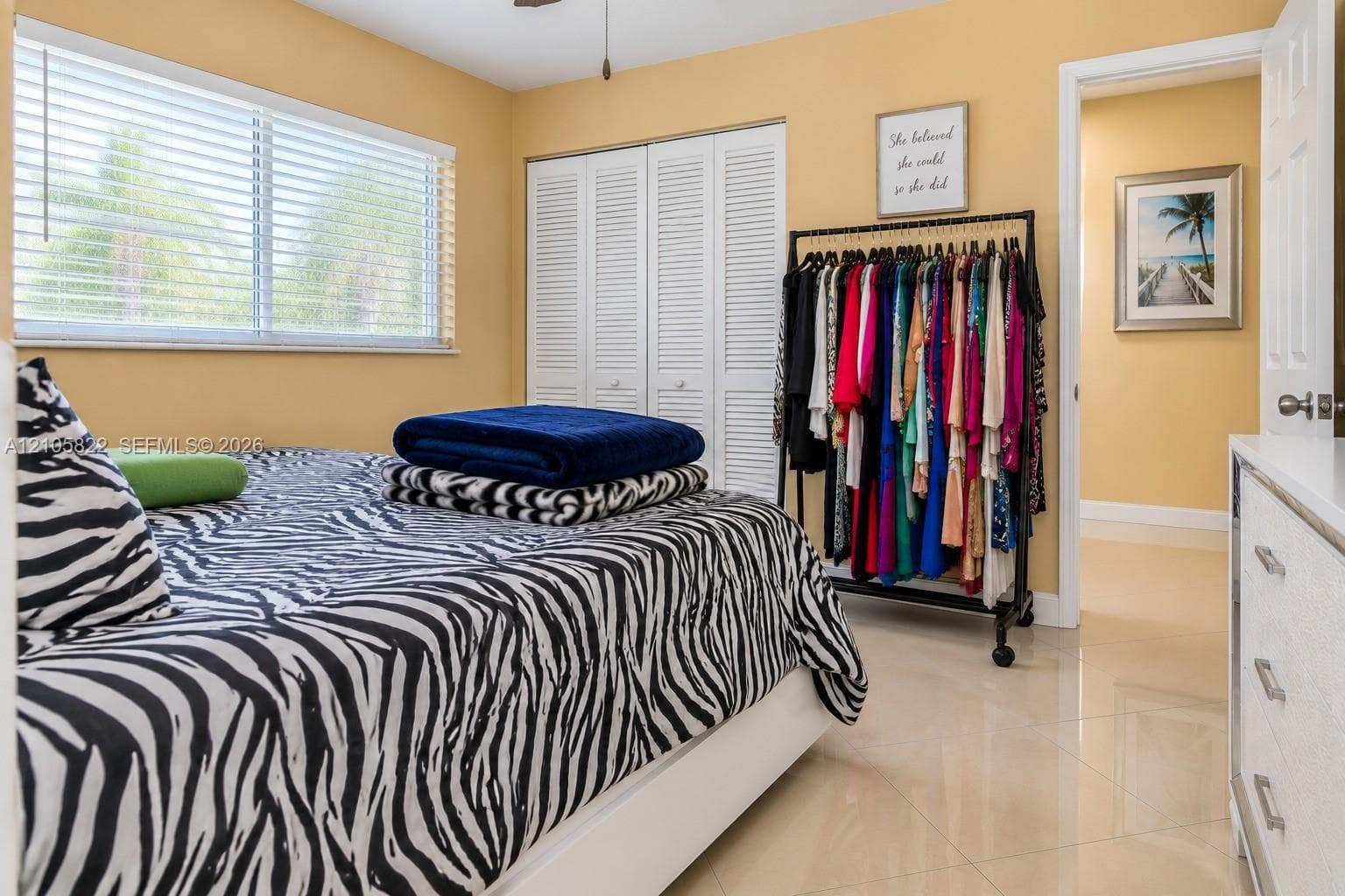 Room interior featuring tile flooring, louvered-style closet doors, and a window with horizontal blinds