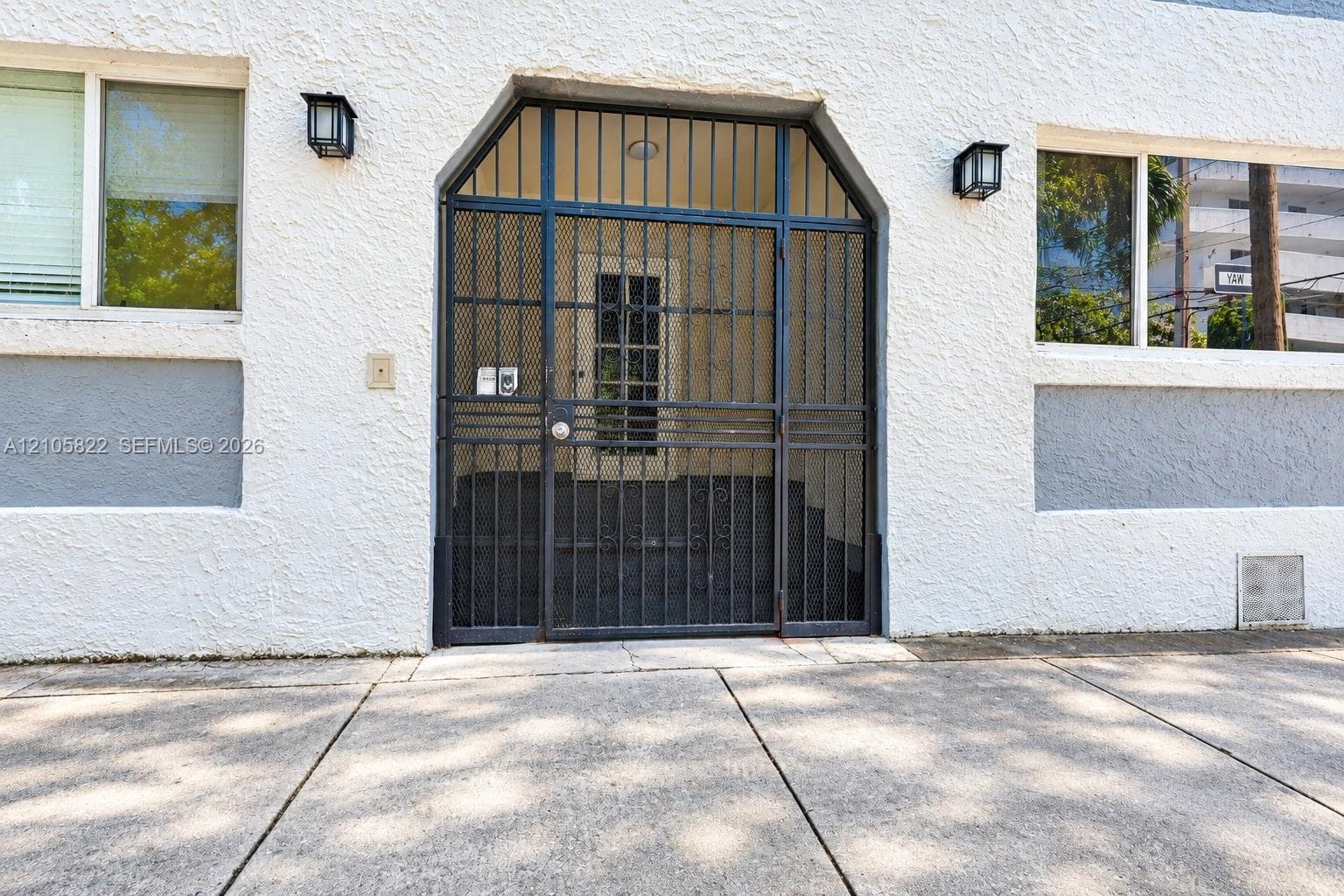 Textured stucco exterior featuring a metal security screen door, multi-pane glass entry door, and wall-mounted exterior lighting fixtures