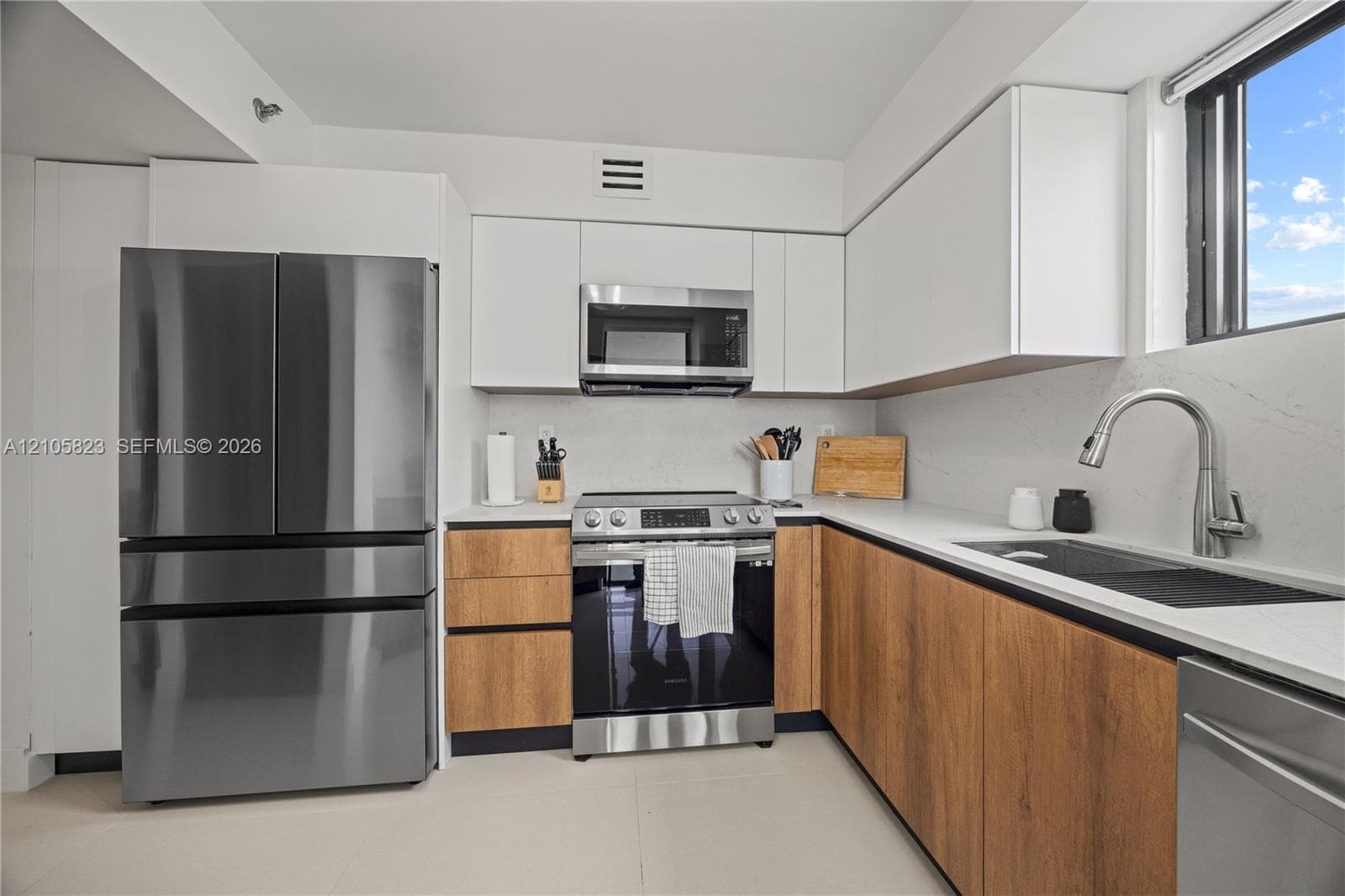 Kitchen featuring two-tone flat-panel cabinetry, stainless steel appliances, white quartz countertops, integrated sink with gooseneck faucet, and porcelain tile flooring