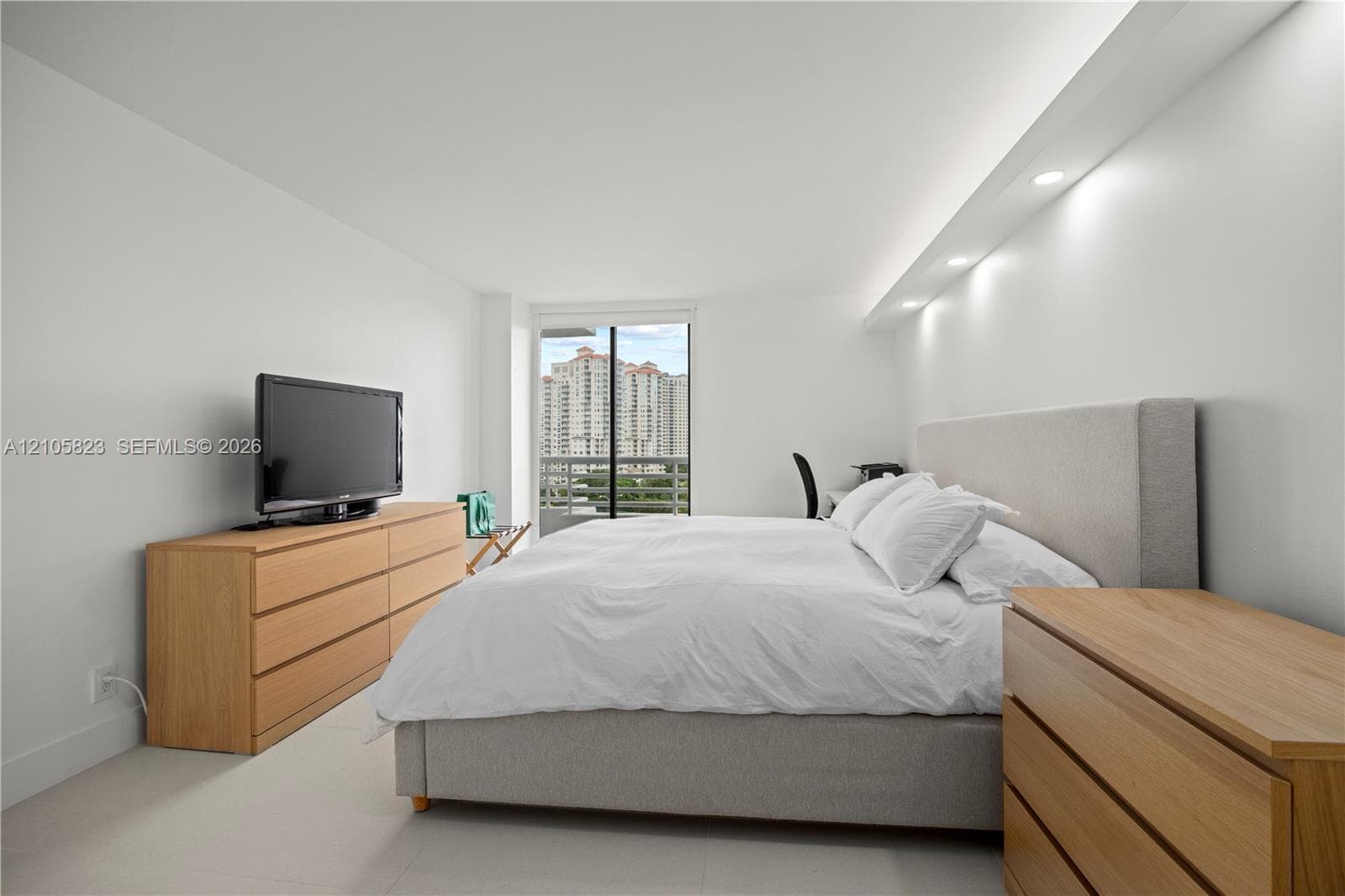 Spacious room featuring neutral tile flooring, recessed cove lighting, and floor-to-ceiling glass sliding doors providing access to a private balcony