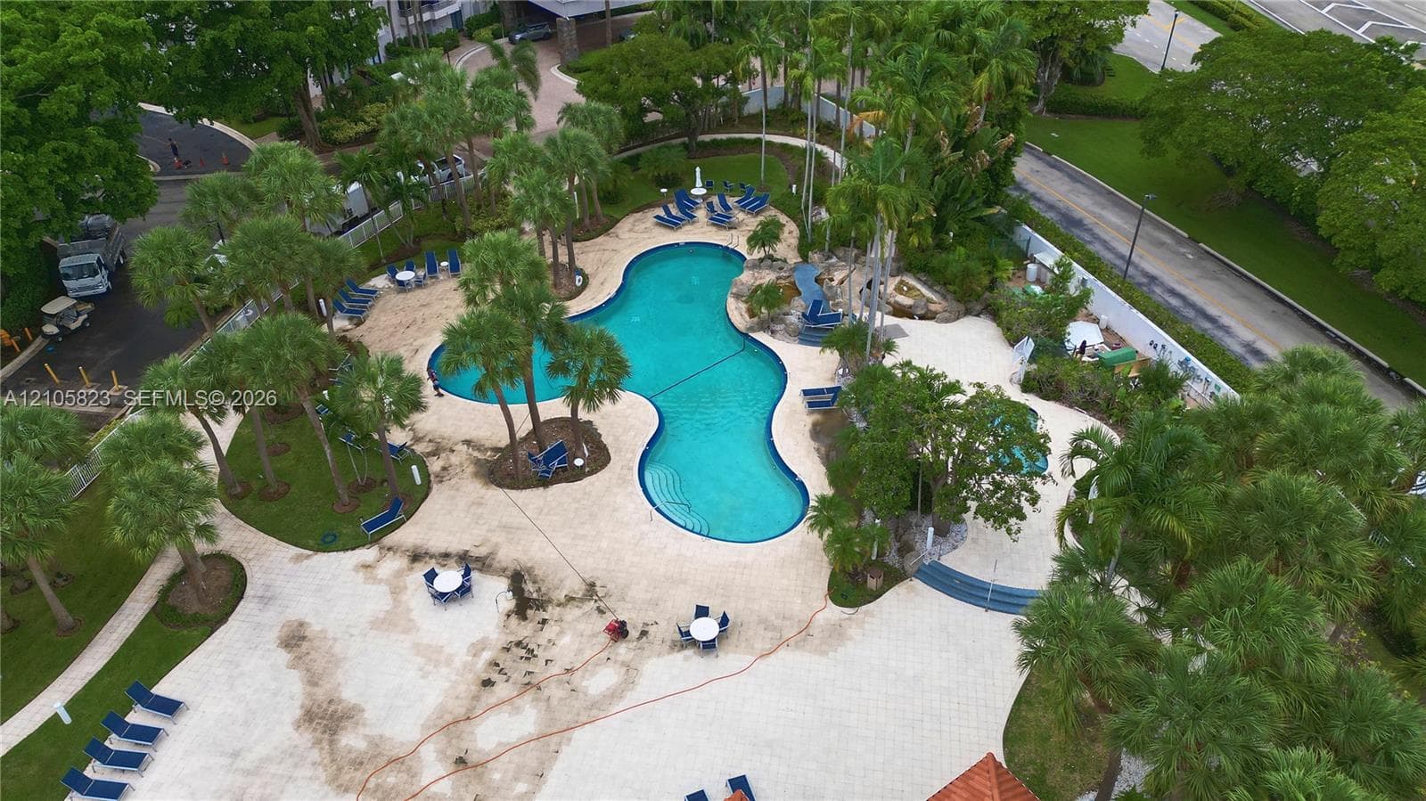 Custom-shaped swimming pool with tiered entry steps, extensive stone paver decking, surrounding palm trees, and mature landscaping