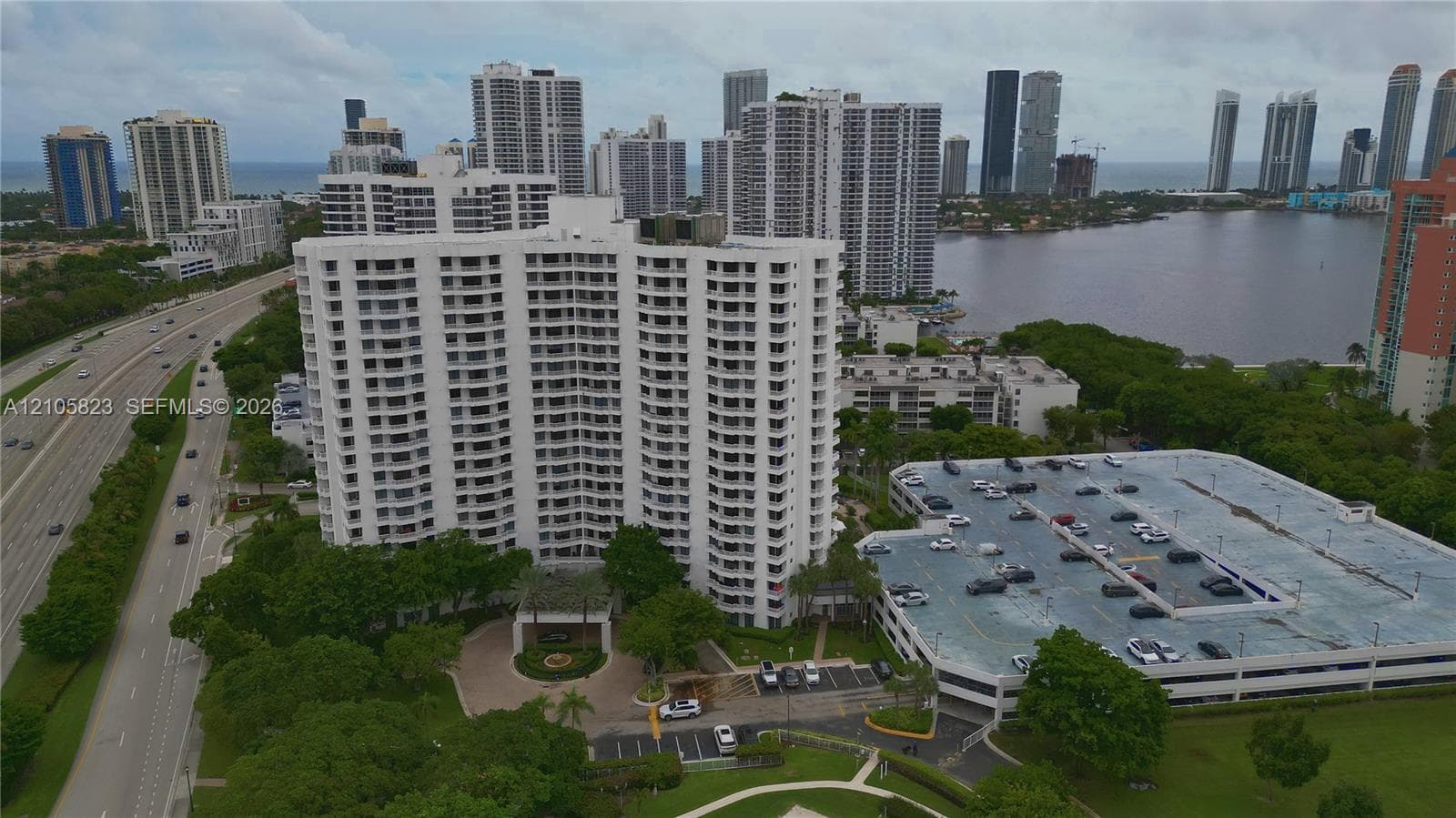 High-rise residential building featuring stacked balconies, a circular porte-cochère, multi-level parking structure, and landscaped grounds