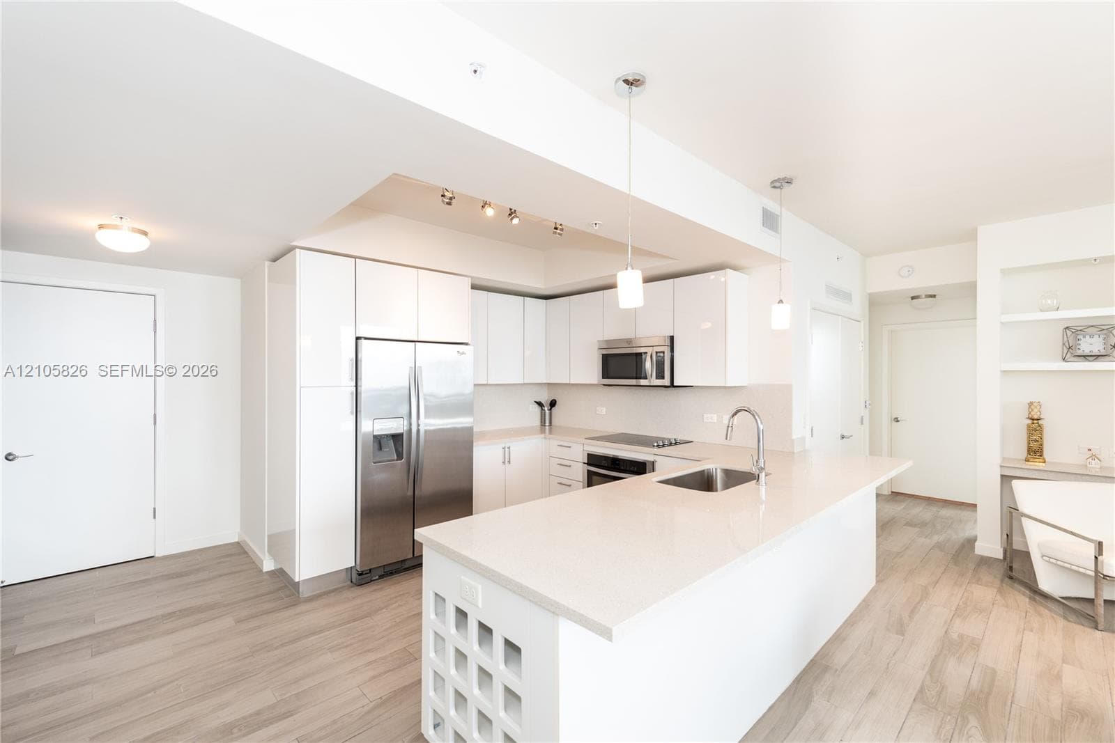 Kitchen featuring high-gloss white cabinetry, a center island with a stone-surface countertop, stainless steel appliances, pendant lighting, and wood-finish flooring