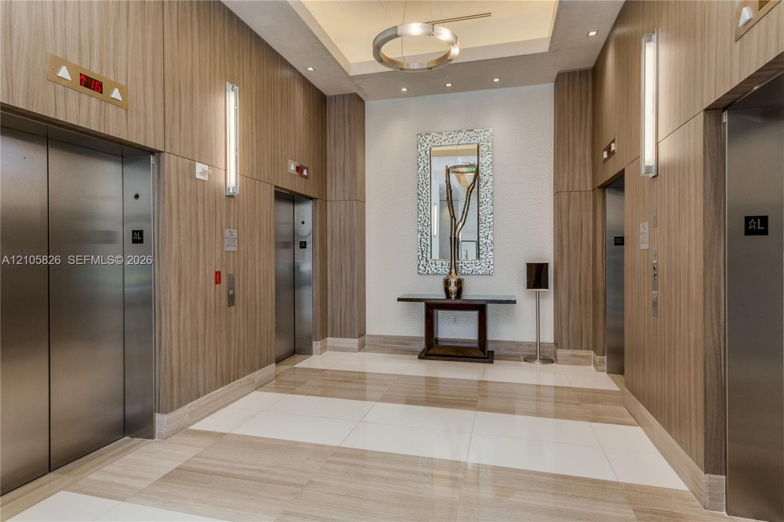 Elevator lobby featuring wood-panel wall cladding, large-format tile flooring, a circular pendant light fixture, and vertical wall-mounted lighting