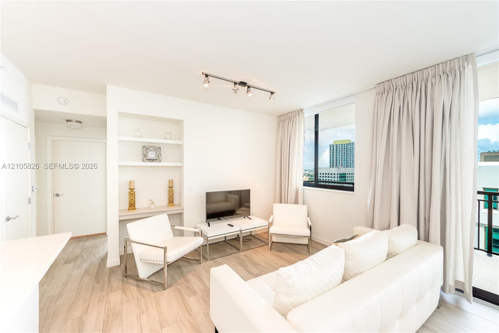Living area featuring wood-finish flooring, built-in shelving, adjustable track lighting, and expansive windows