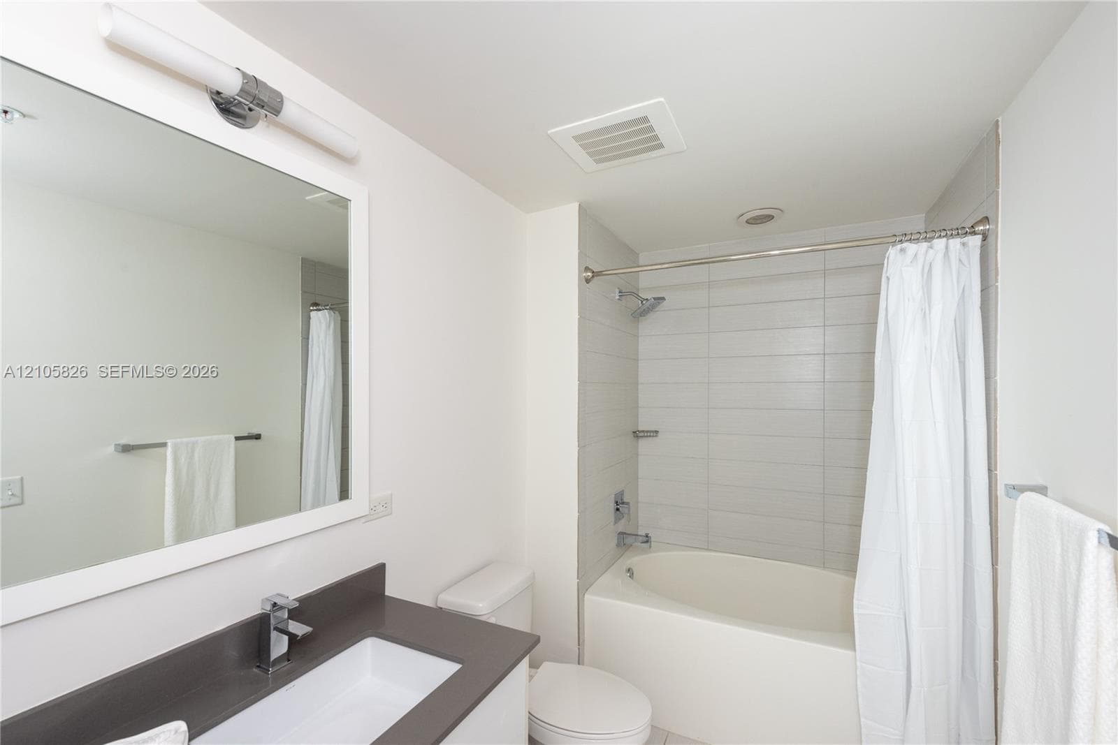 Bathroom featuring a dark-toned vanity countertop, white rectangular undermount sink, wall-mounted light fixture, and a tub with a tiled surround