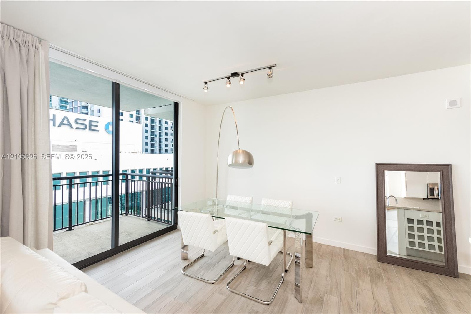 Floor-to-ceiling sliding glass door, private balcony with metal railing, wood-finish flooring, and multi-bulb track lighting