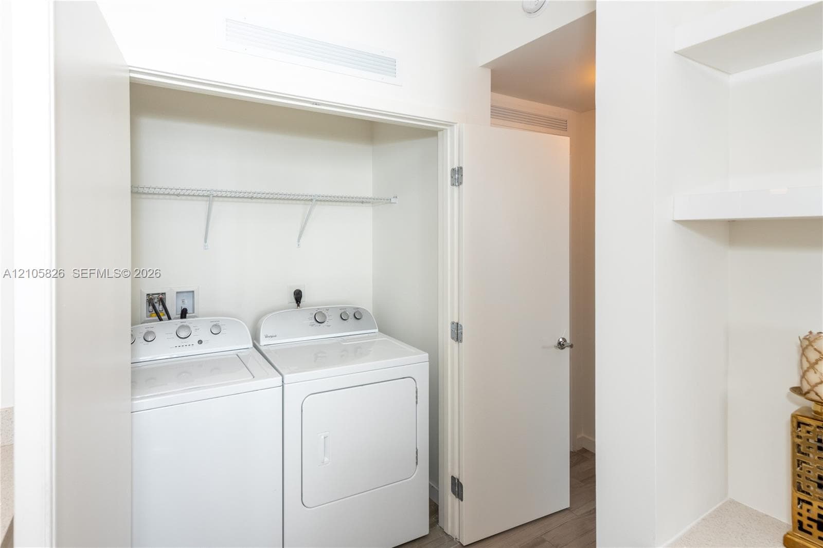 Dedicated utility area featuring built-in shelving, white cabinetry, integrated laundry hookups, and wood-finish flooring