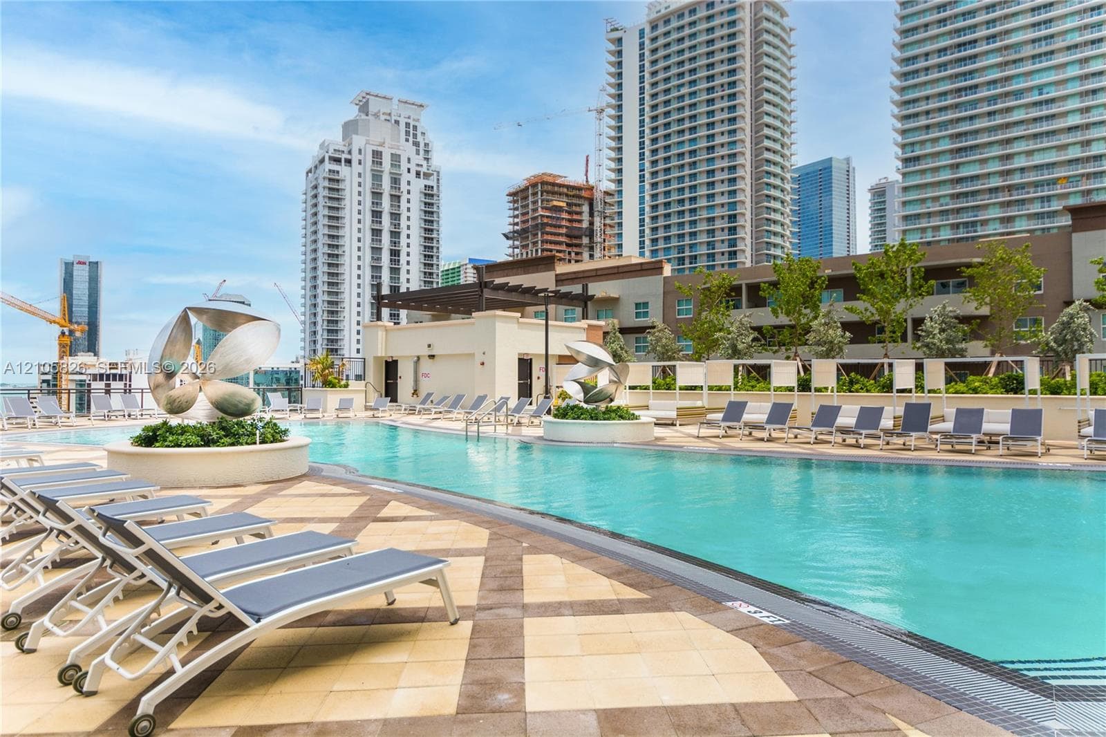 Swimming pool with patterned tile decking, metal sculptural elements, integrated planters, and structured pergolas