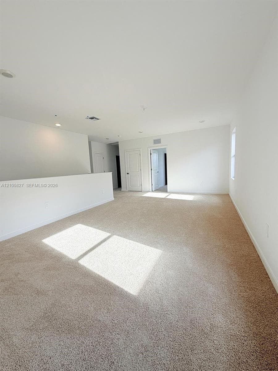 Expansive carpeted room featuring a half-wall partition, neutral wall tones, recessed lighting, and multi-panel interior doors