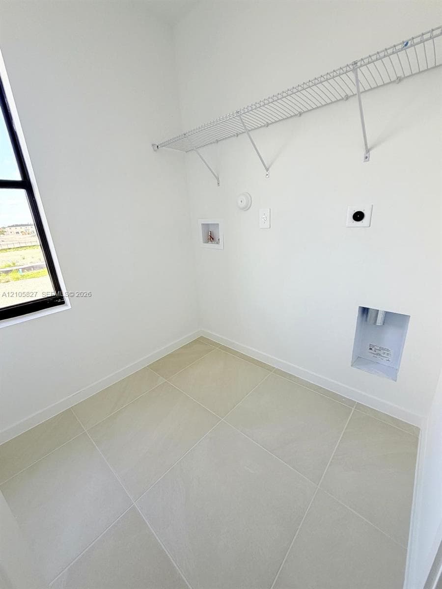 Utility space featuring large-format ceramic tile flooring, a window with a black frame, and white wire shelving