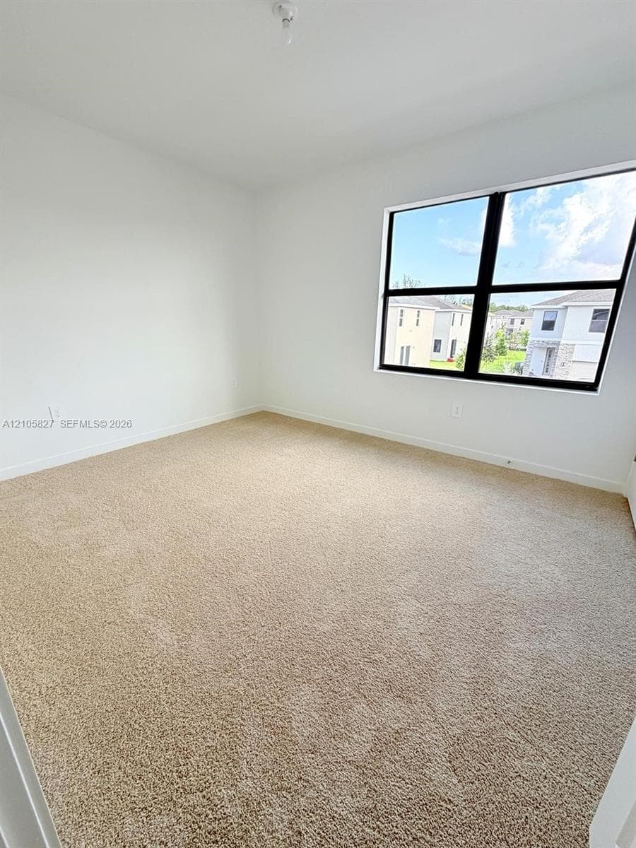 Neutral interior room featuring neutral carpeting, white walls, and a large black-framed window
