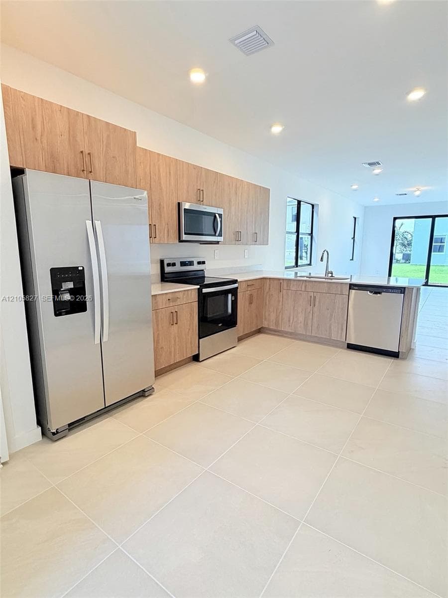 Kitchen featuring wood-finish cabinetry, stainless steel appliances, neutral tile flooring, and recessed lighting