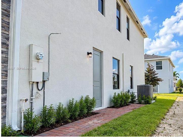 Stucco exterior featuring vertical windows, a paver walkway, and structured landscaping