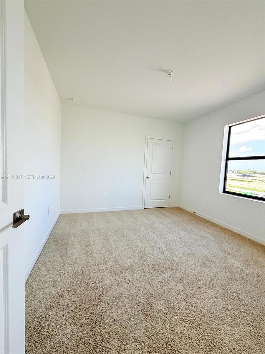 Interior space featuring wall-to-wall carpeting, neutral-toned walls, and a window with dark-finished framing