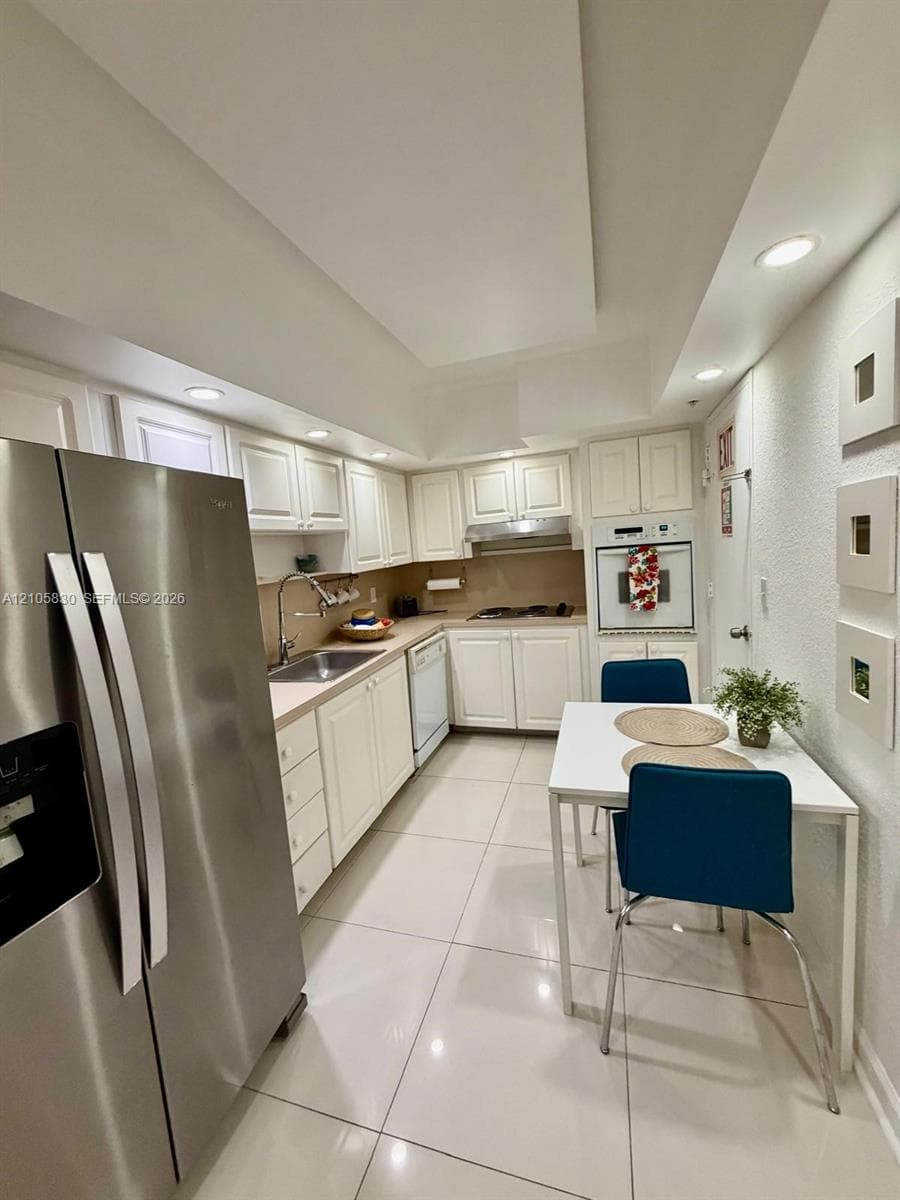 Kitchen featuring white cabinetry, stainless steel appliances, recessed ceiling lighting, and large-format tile flooring