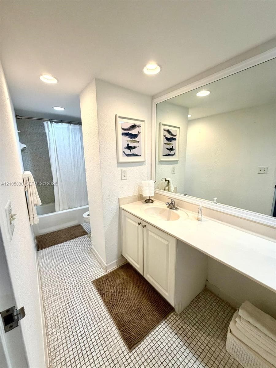 Bathroom featuring a large vanity with integrated countertop and sink, expansive wall-mounted mirror, recessed lighting, and a combination tub and shower enclosure with a tiled surround
