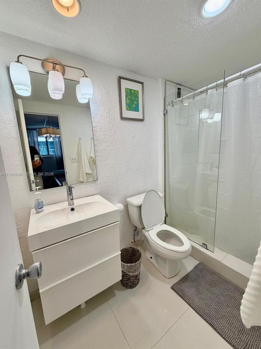 Modern floating vanity with an integrated sink and chrome faucet, rectangular wall mirror, three-light fixture, and a glass-enclosed shower featuring tile surround
