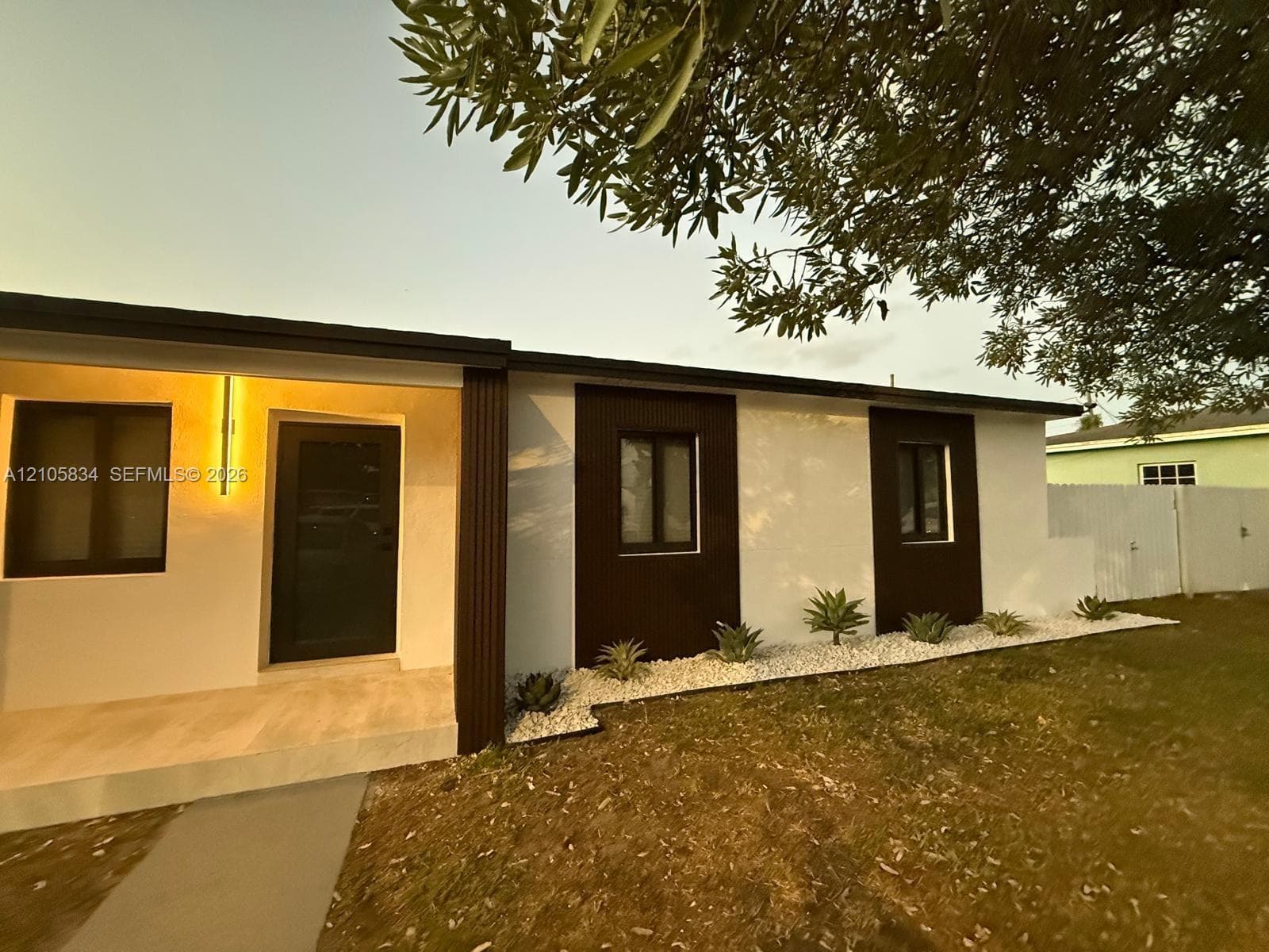 Exterior facade featuring two-tone stucco and vertical siding, covered entryway, stone-tiled porch, and landscaped bed with gravel and agave