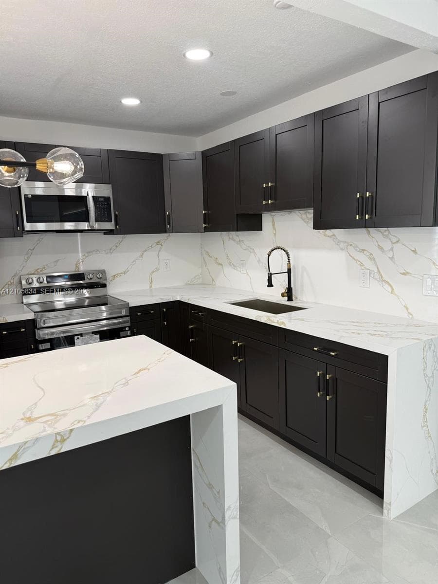 Kitchen featuring dark Shaker-style cabinetry, white waterfall-edge countertops with gold veining, stainless steel appliances, and a matte black gooseneck faucet