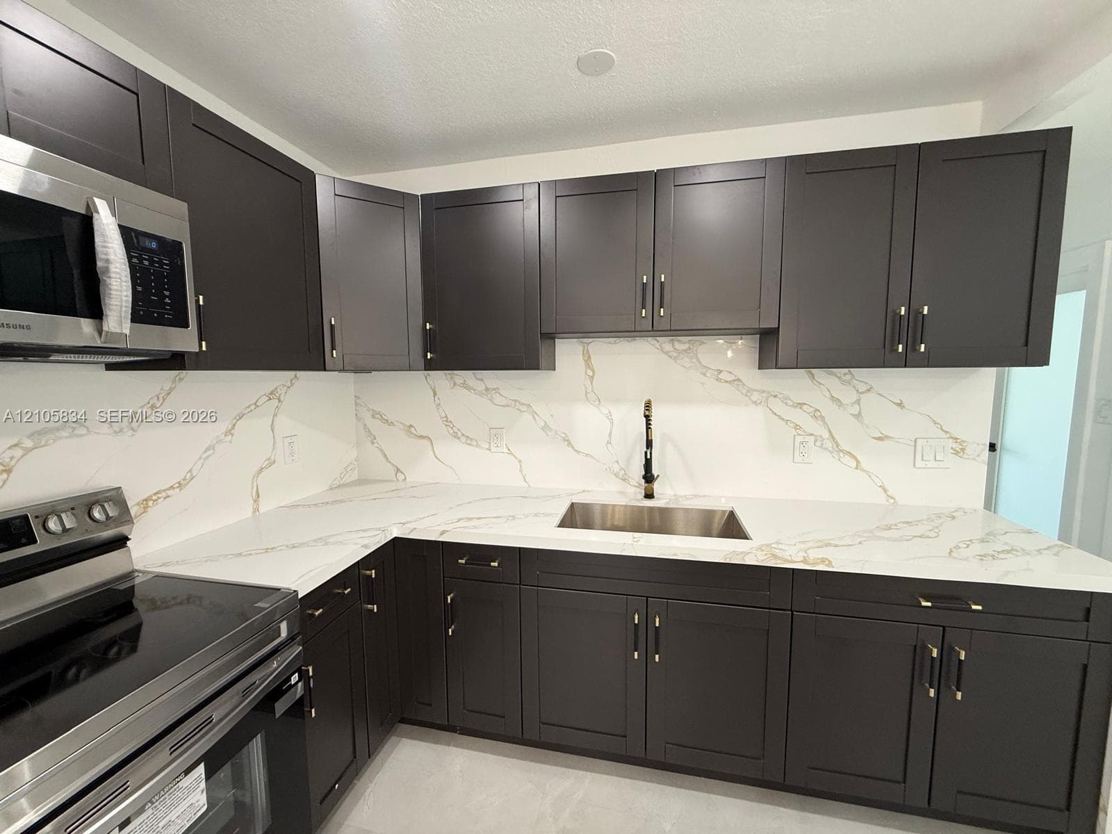 Kitchen featuring dark shaker-style cabinetry, quartz countertops with integrated backsplash, stainless steel undermount sink, matte black hardware, and stainless steel appliances