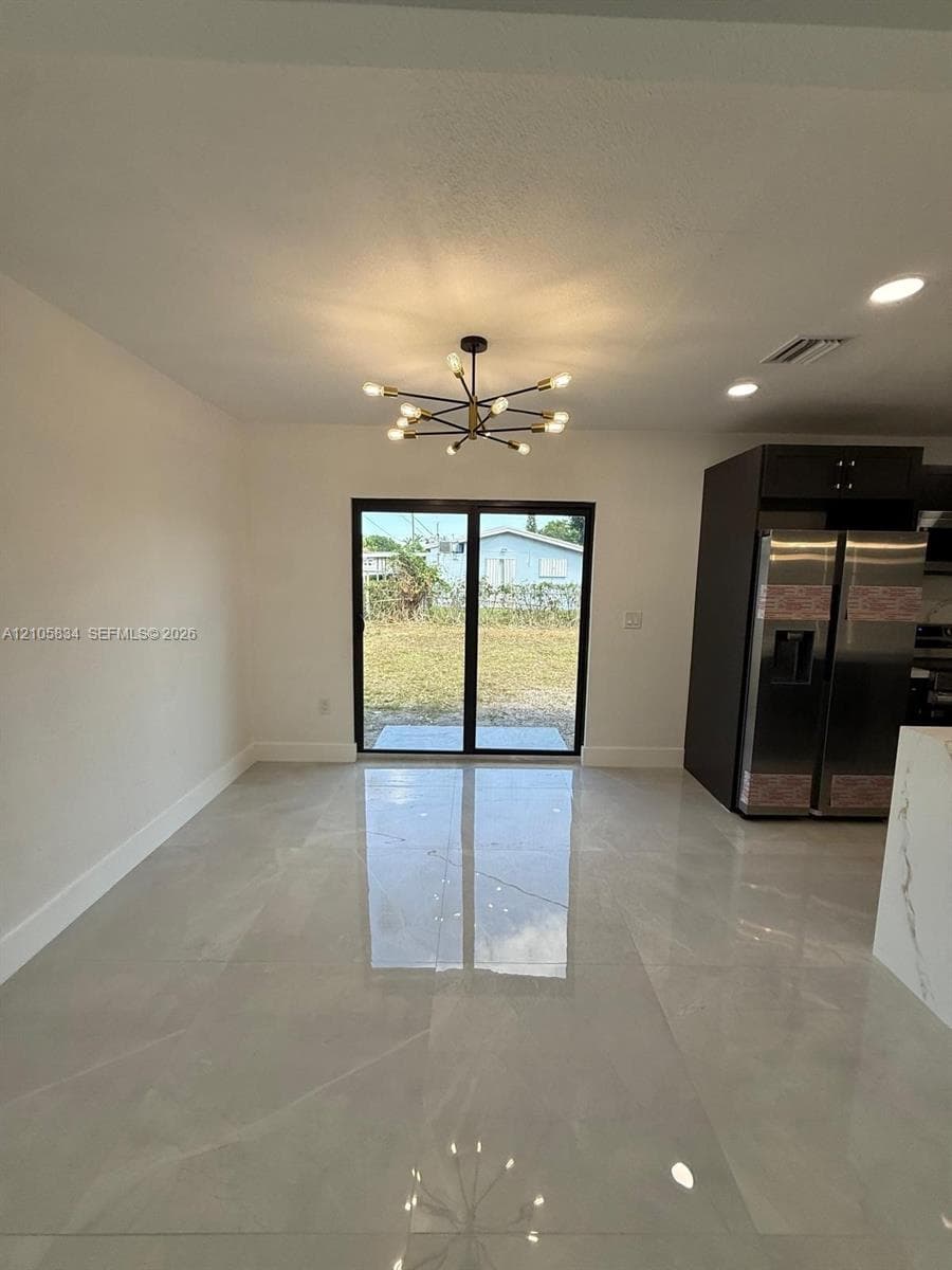 Large-format light tile flooring, multi-arm sputnik-style chandelier, black-framed sliding glass doors, dark-toned cabinetry, and stainless-steel double-door refrigerator