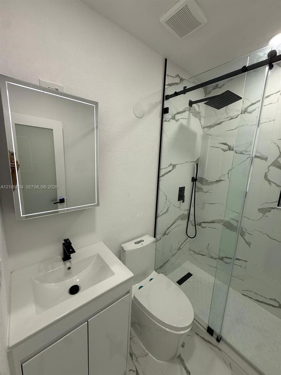 Bathroom featuring a vanity with an integrated sink, matte black faucet, and LED-backlit mirror