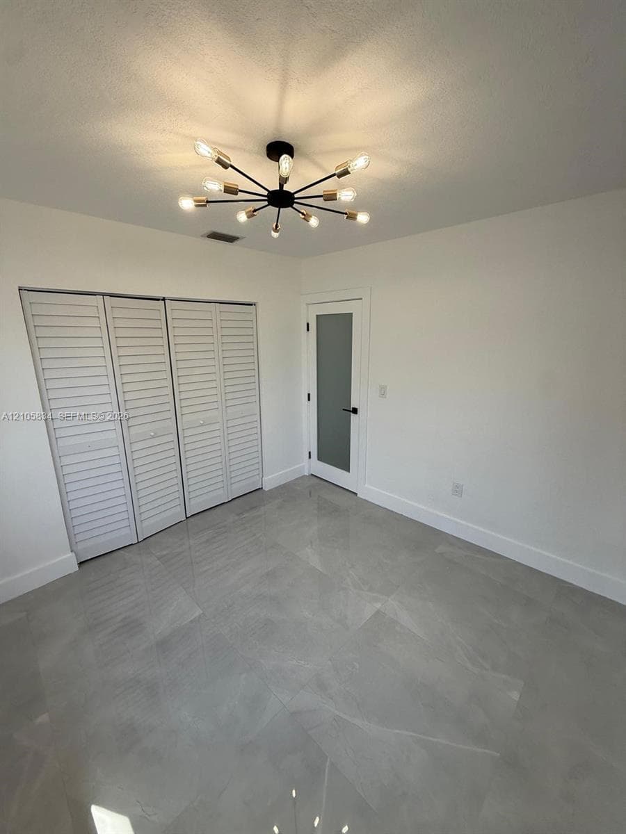 Polished large-format tile flooring, modern multi-arm sputnik chandelier, tri-fold louvered closet doors, and single-panel door with frosted glass insert