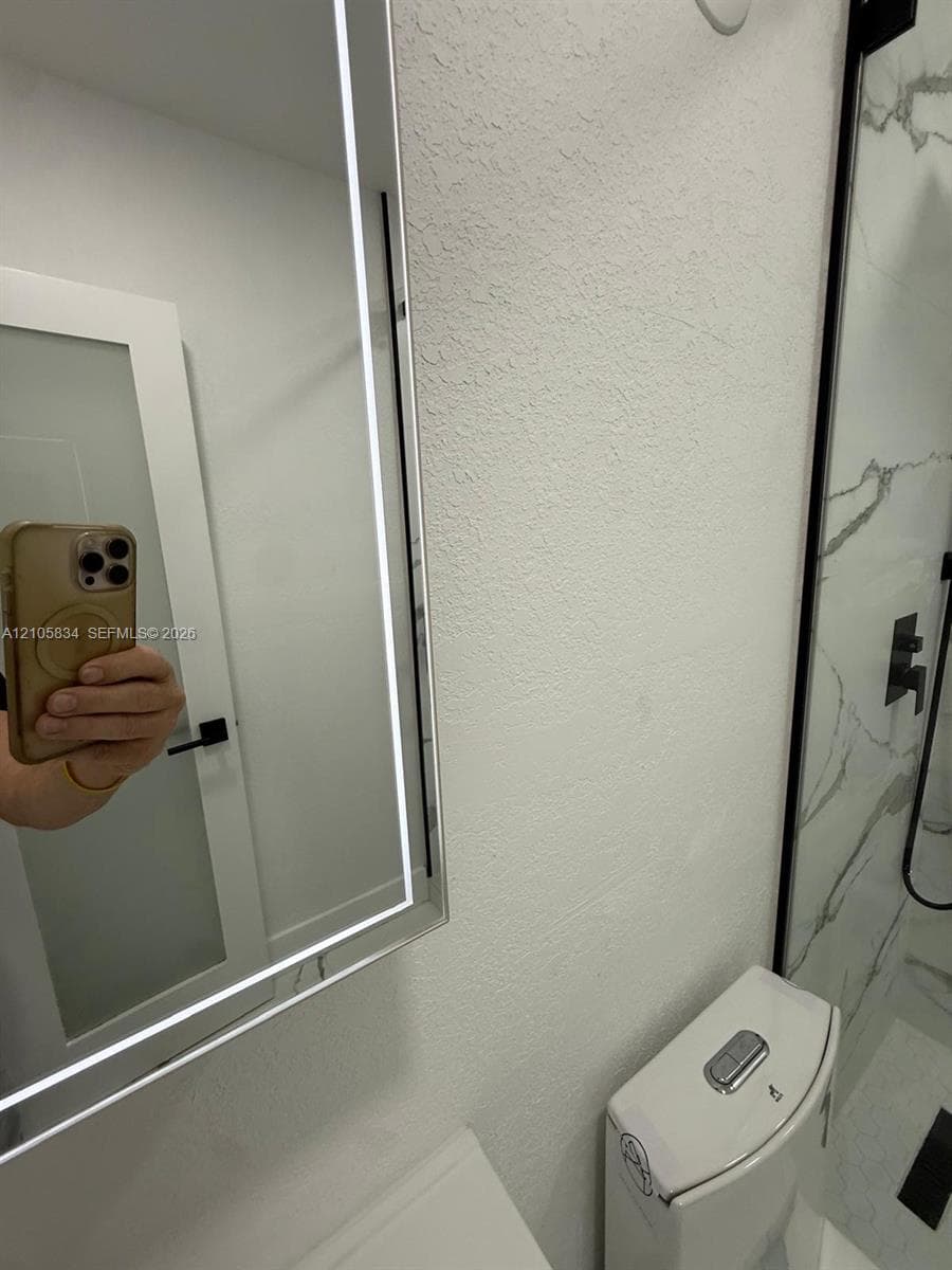 Illuminated LED vanity mirror, dual-flush toilet, and walk-in shower featuring large-format veined tile surround and matte black hardware