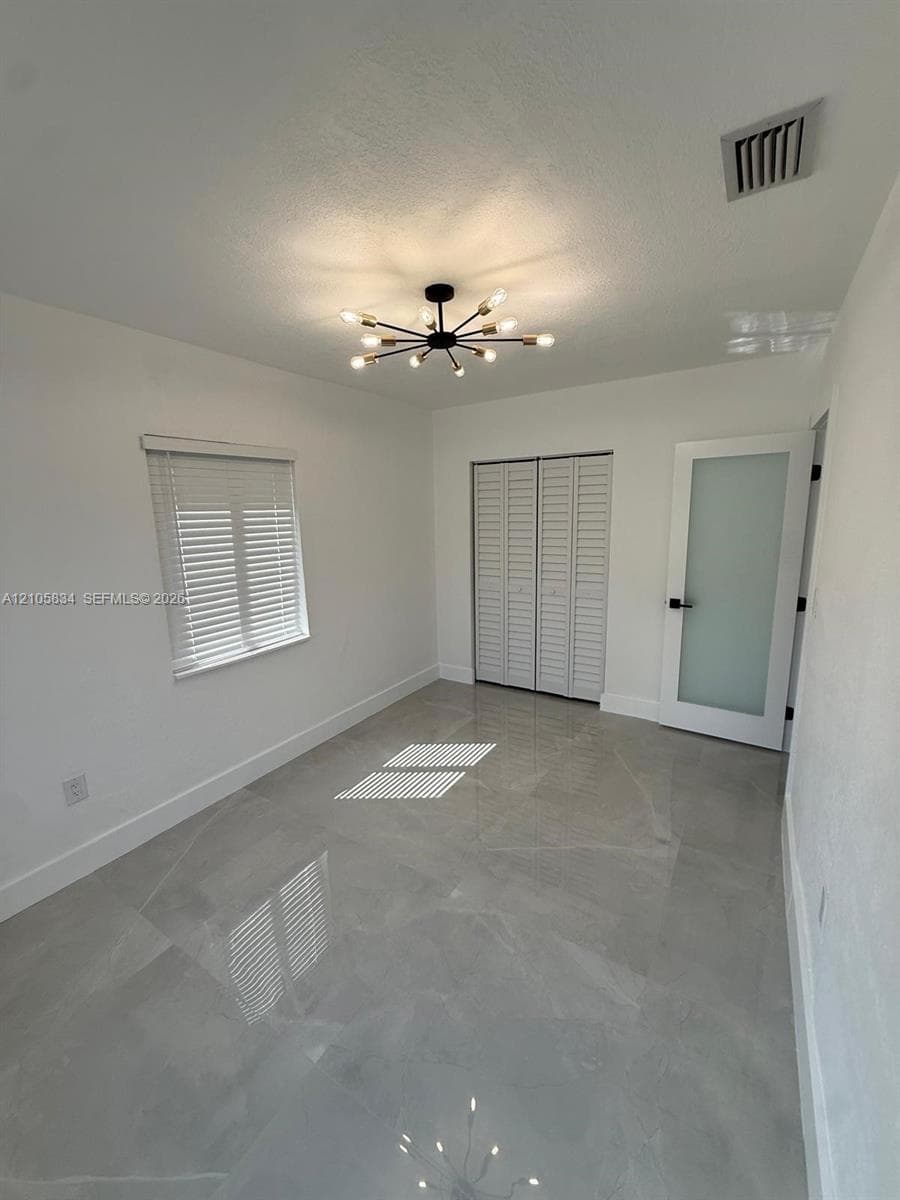 Large-format tile flooring, modern multi-arm sputnik chandelier, frosted glass panel door with matte black hardware, and bi-fold louvered closet doors