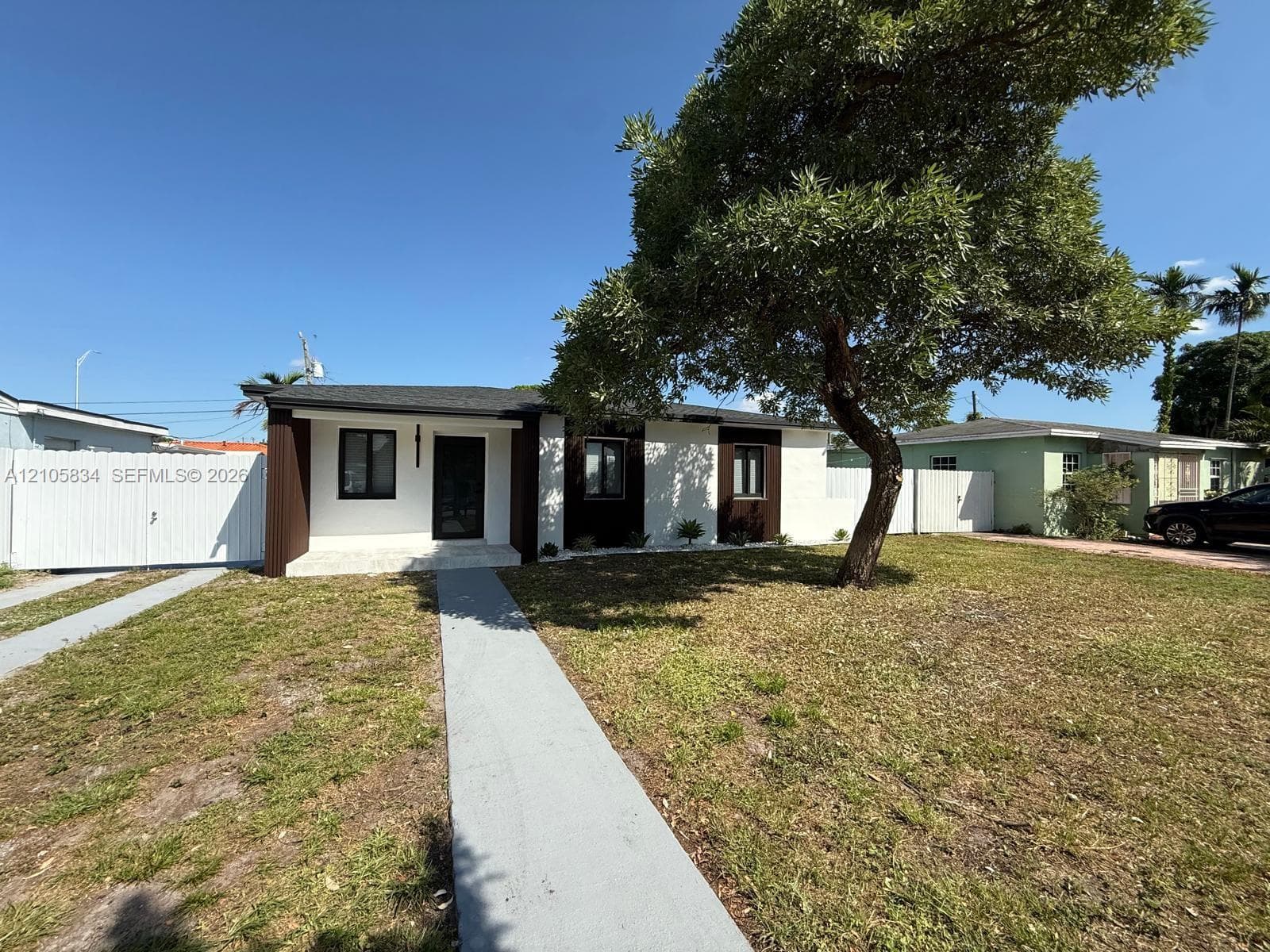 Single-story exterior featuring a high-contrast facade, dark-toned trim, a concrete walkway, and white privacy fencing