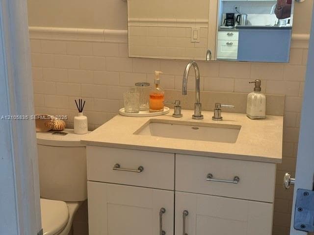 White vanity with a neutral solid-surface countertop, undermount sink, chrome gooseneck faucet, and white subway tile wall backsplash