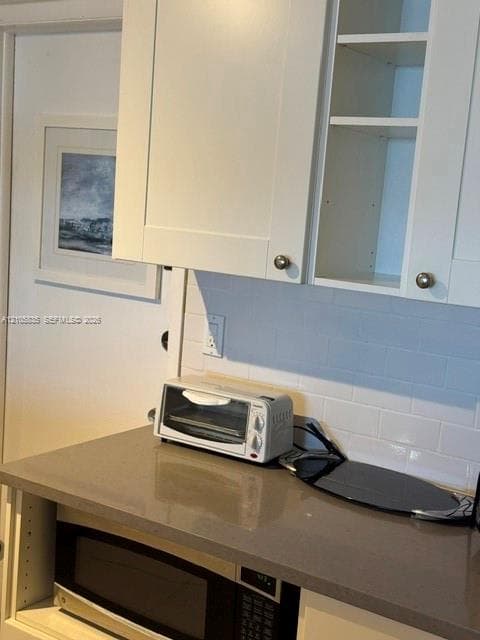 White shaker-style cabinetry, neutral-toned solid surface countertop, white subway tile backsplash, and built-in microwave