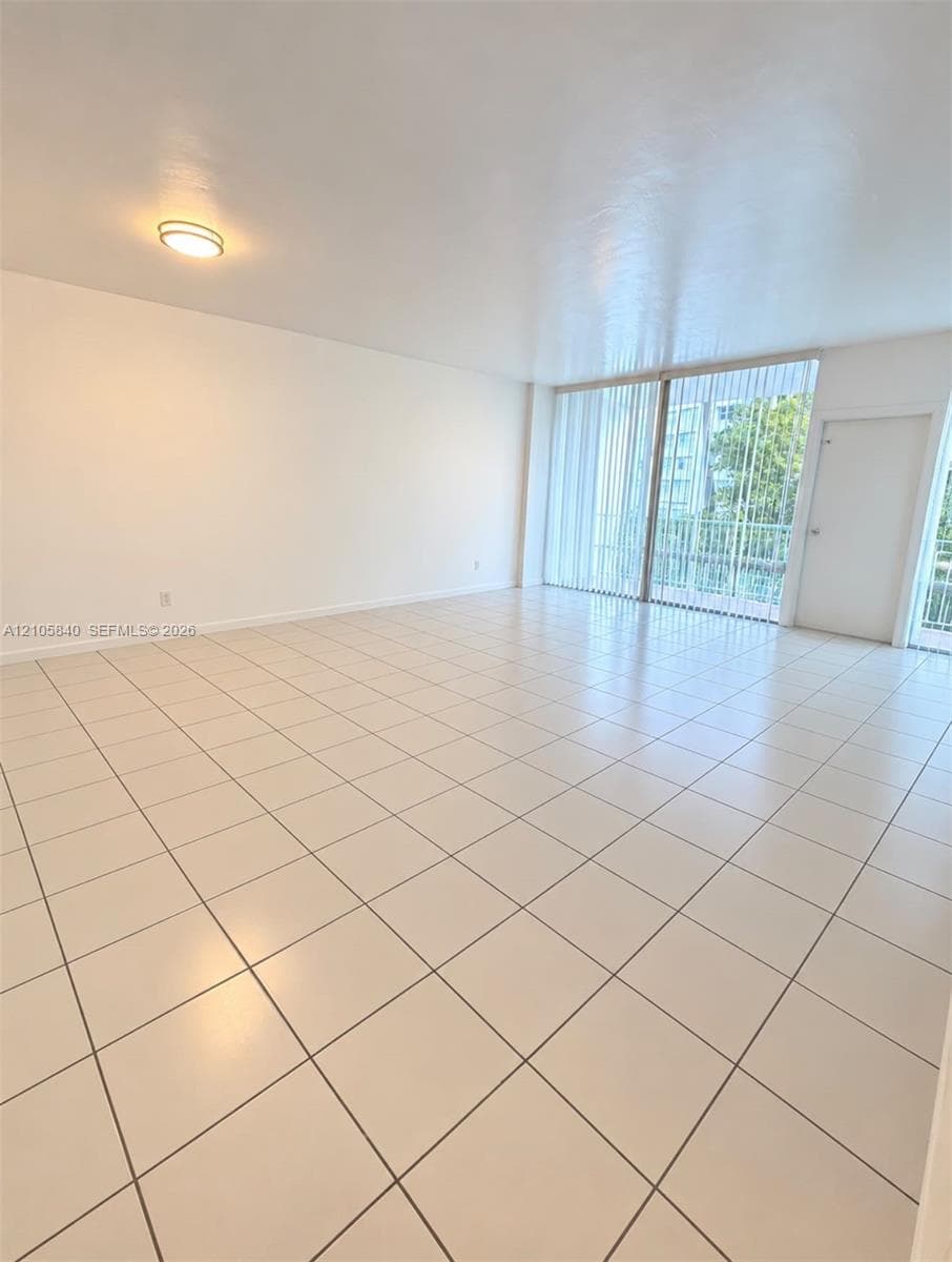 Open-concept space featuring light-toned tile flooring, flush-mount lighting, and floor-to-ceiling glass sliding doors with vertical blinds