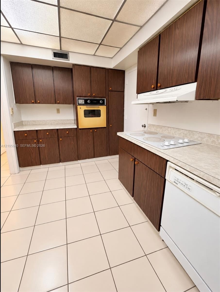 Kitchen featuring flat-panel wood-finish cabinetry, solid-surface countertops, a built-in wall oven, a drop-in electric cooktop, and ceramic tile flooring