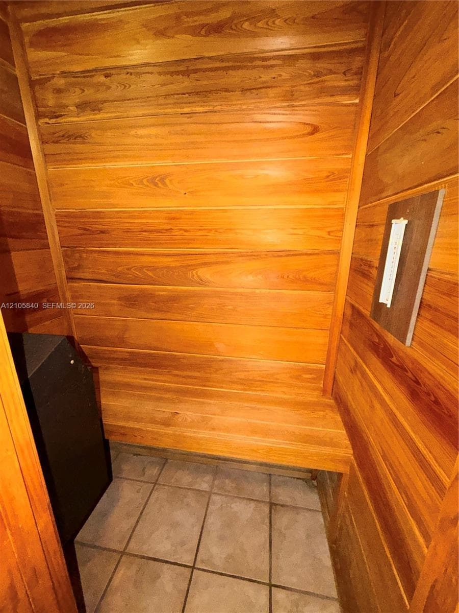 Sauna featuring natural wood-paneled walls, built-in wooden bench seating, tiled flooring, and a dedicated heating unit