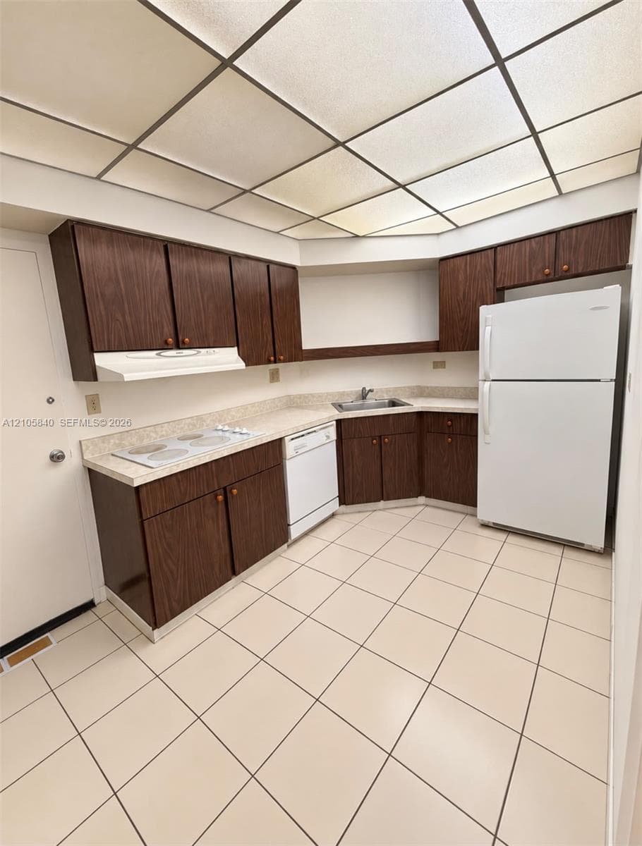 Kitchen featuring wood-finish cabinetry, solid-surface countertops, integrated cooktop, and large-format tile flooring