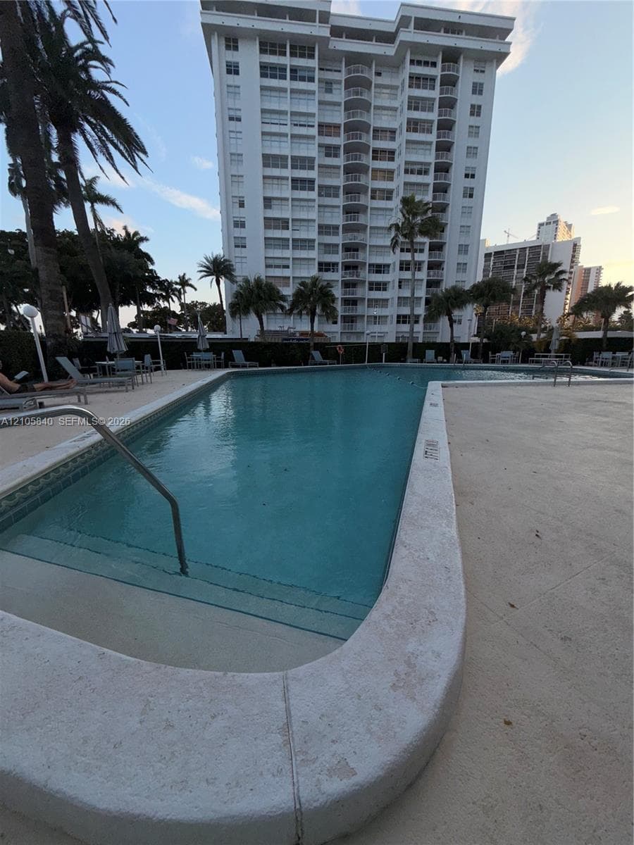 In-ground swimming pool featuring stone coping and integrated steps, surrounded by a paved deck and mature palm trees