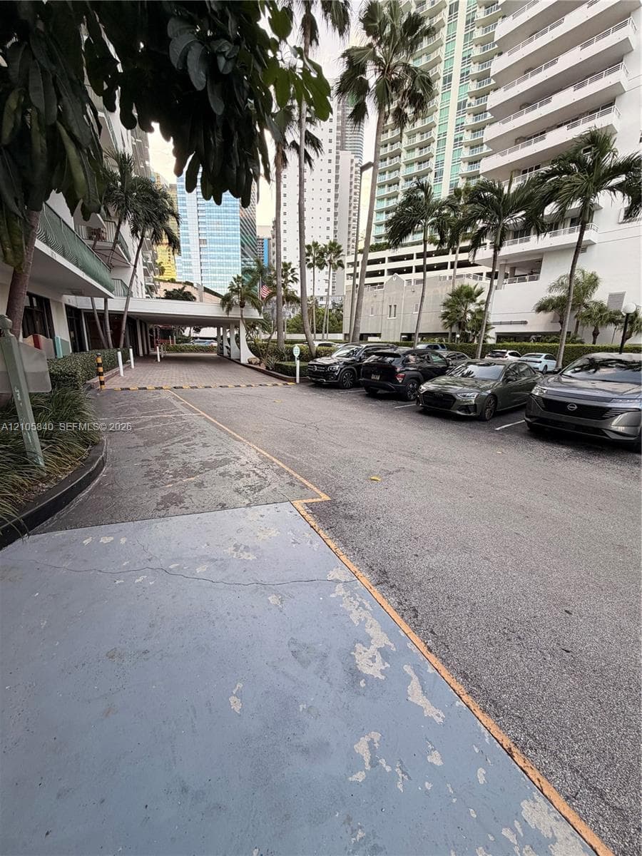 Paved surface parking area featuring palm tree landscaping and a covered porte-cochère
