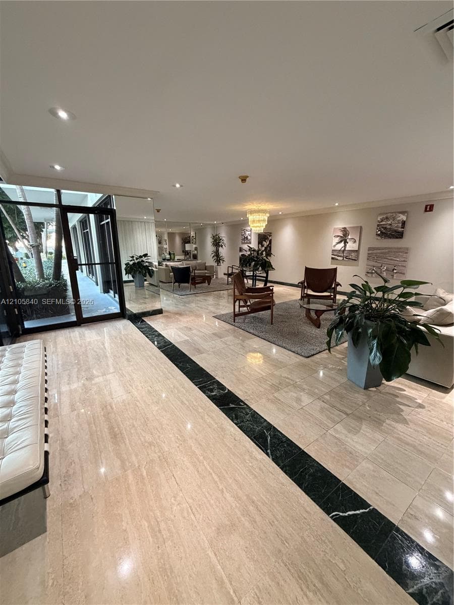Expansive lobby featuring polished stone flooring with a black stone inlay, full-height glass-paneled entry door, recessed lighting, and wall-mounted tiered crystal chandelier
