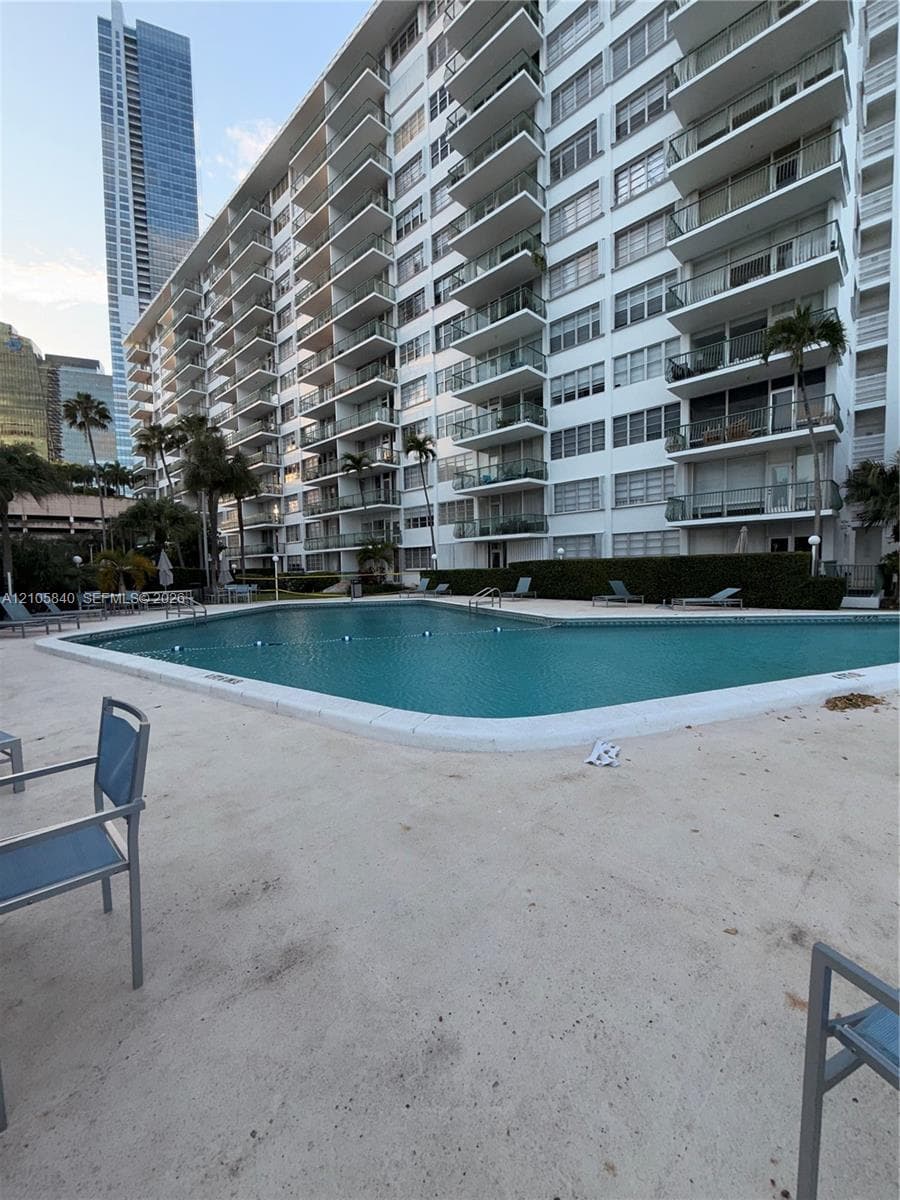 Swimming pool with concrete pool deck, perimeter landscaping, and multi-story residential building with private balconies
