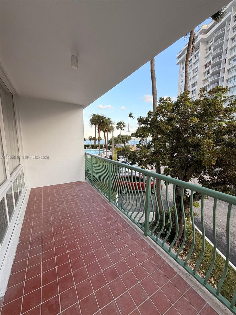 Covered balcony featuring red tile flooring and a decorative metal railing
