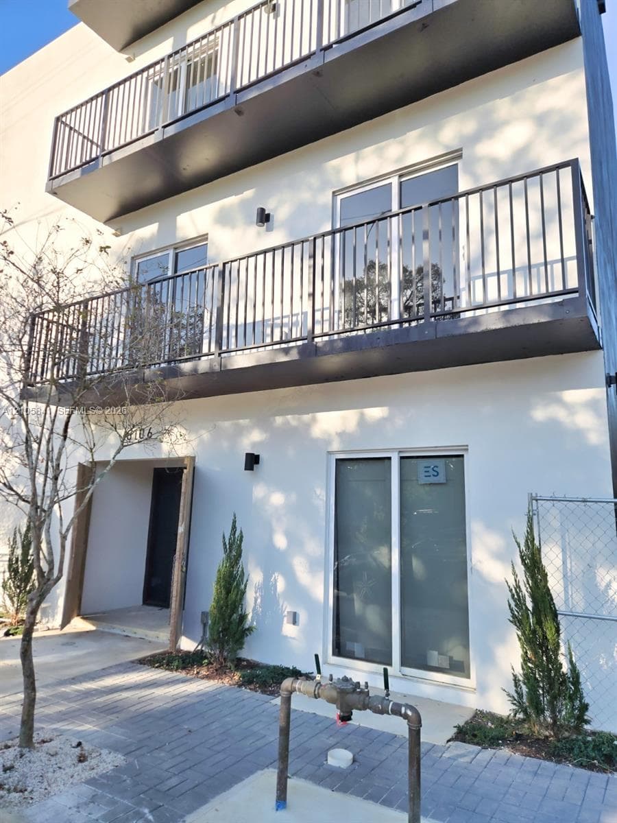 Multi-story exterior featuring smooth stucco siding, dual stacked balconies with metal railings, sliding glass doors, and a paver stone walkway