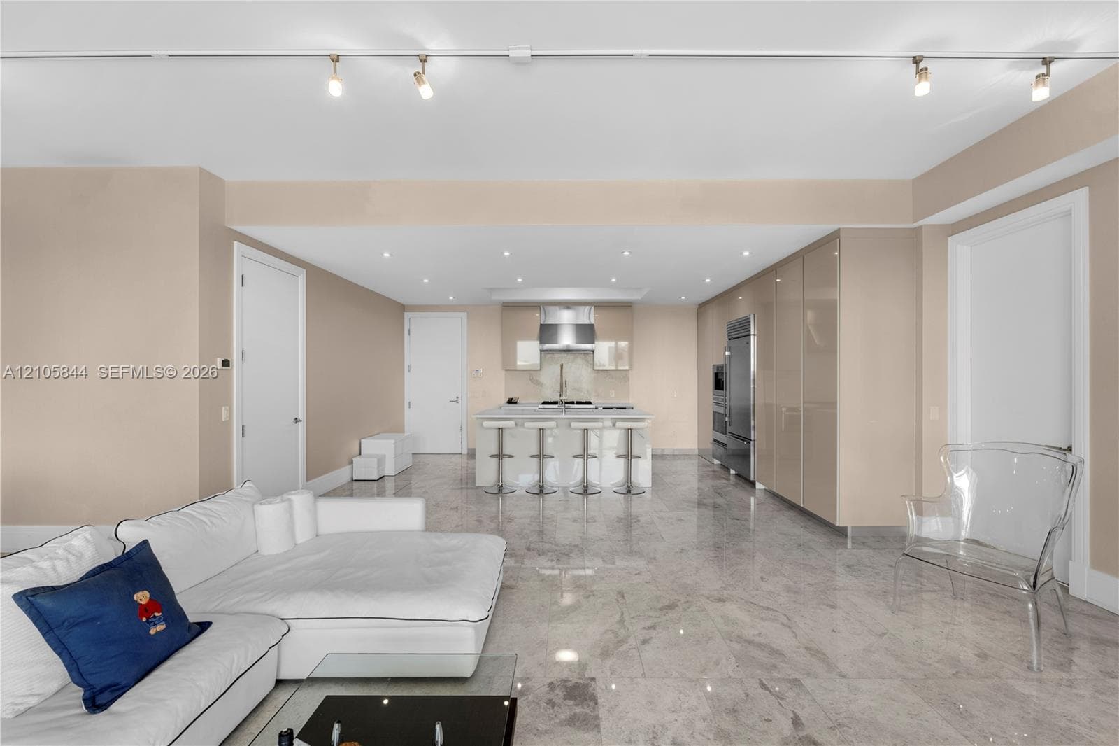 Kitchen featuring high-gloss cabinetry, a stone-topped island with a stainless steel range hood, stone flooring, and adjustable track lighting