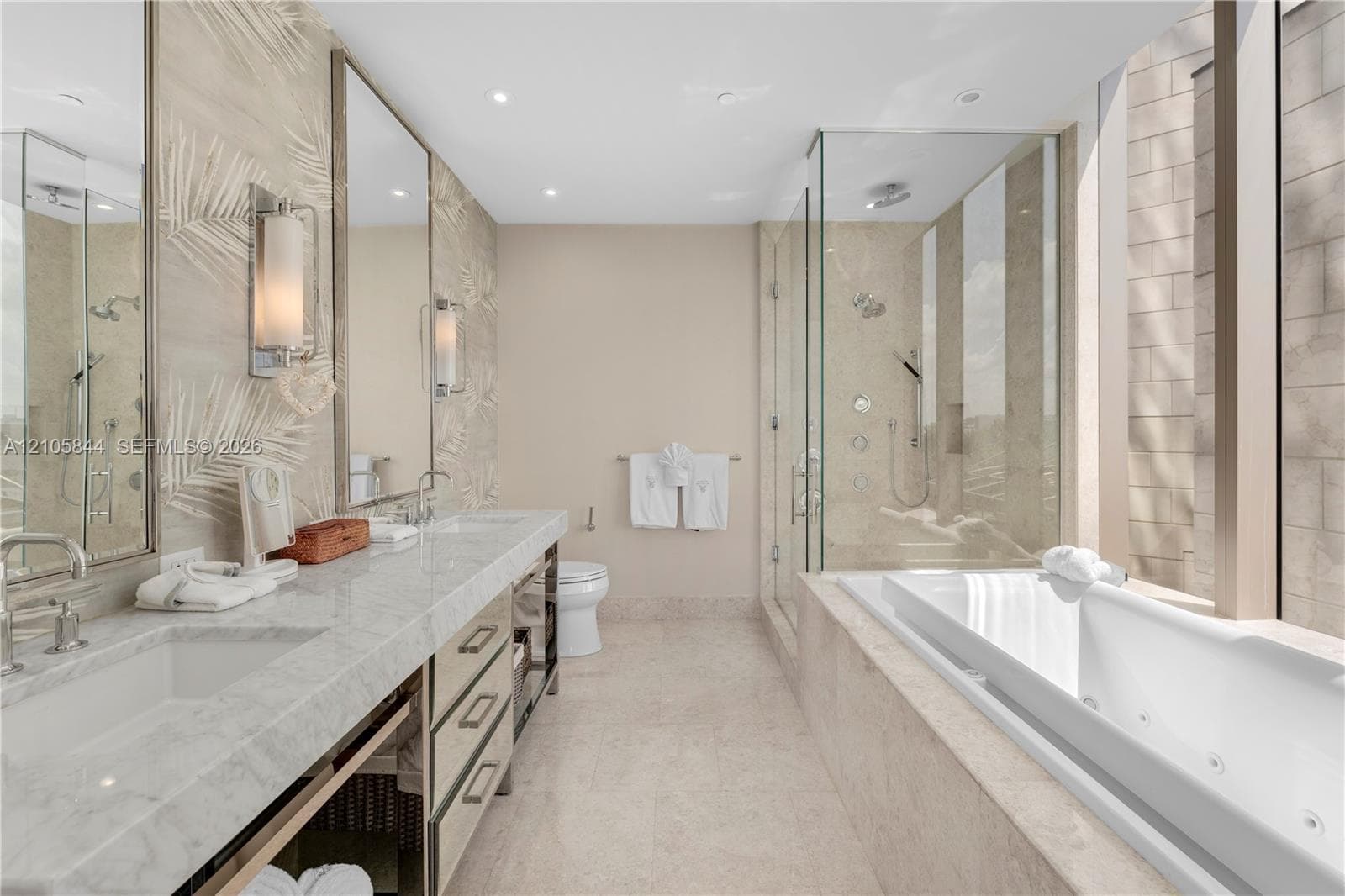 Dual vanity with stone-surfaced countertop, frameless glass-enclosed shower featuring multi-head fixtures, and built-in jetted soaking tub