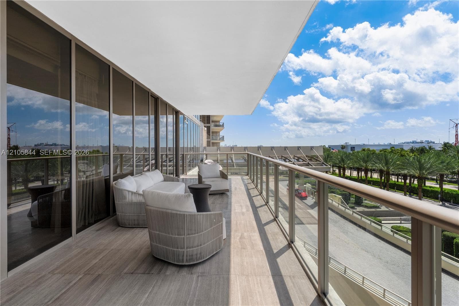 Expansive covered balcony featuring floor-to-ceiling glass paneling, wood-finish flooring, and a glass-paneled railing with a metal handrail