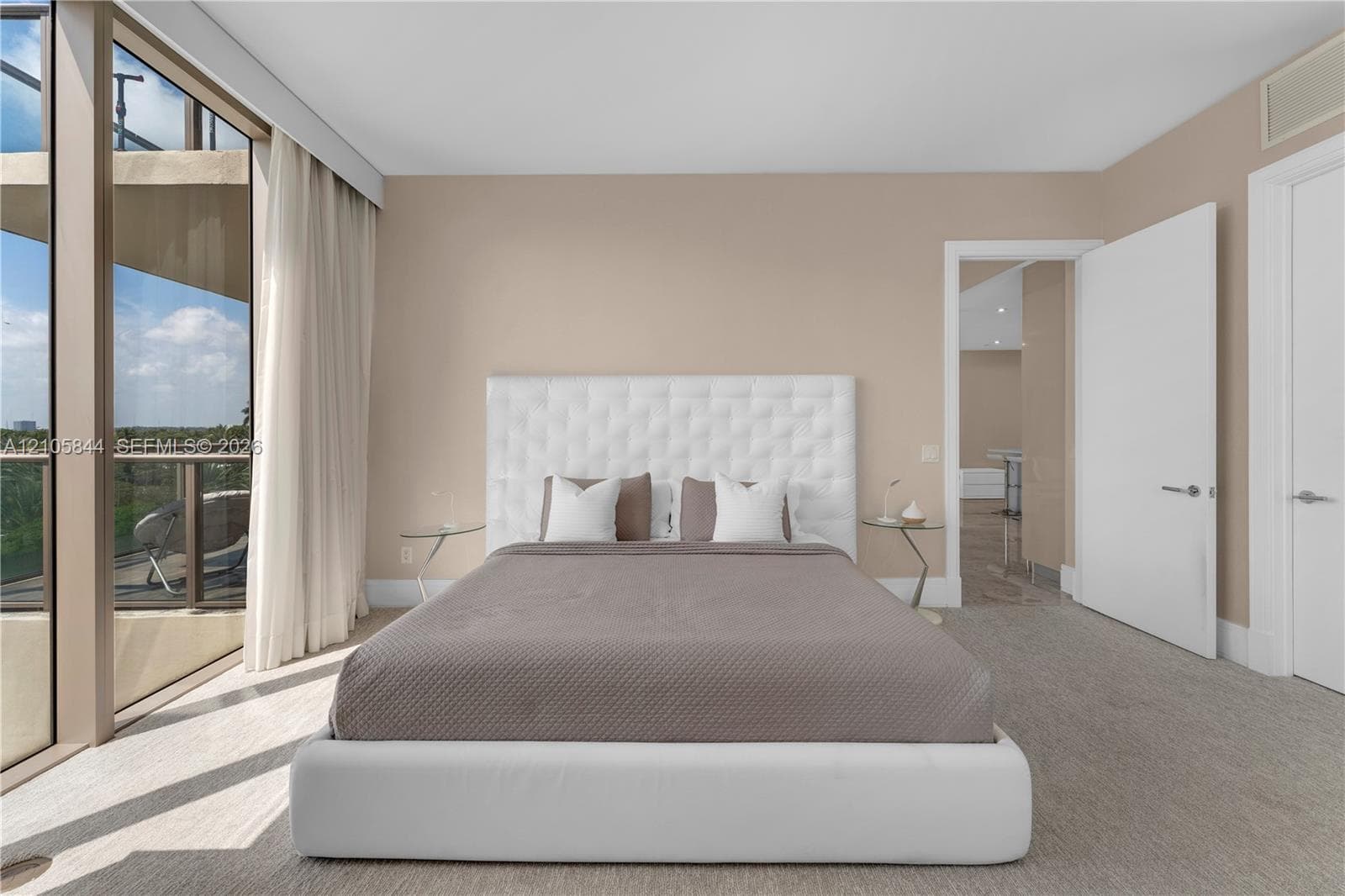 Floor-to-ceiling glass wall, private balcony with metal railing, neutral carpeting, and solid-core interior doors