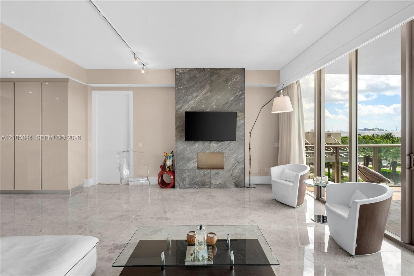 Full-height stone fireplace surround, floor-to-ceiling glass panel walls, polished stone flooring, and integrated wall cabinetry