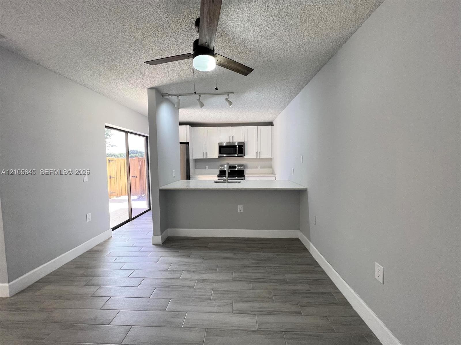 Kitchen featuring white cabinetry, stainless steel appliances, a peninsula counter with a sink, wood-finish tile flooring, and a ceiling fan with integrated lighting