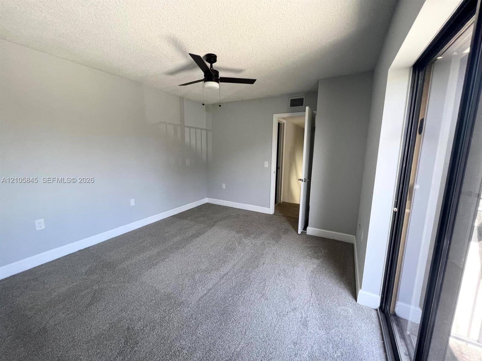 Interior space featuring neutral wall tones, wall-to-wall carpeting, a black ceiling fan with integrated lighting, and a sliding glass door